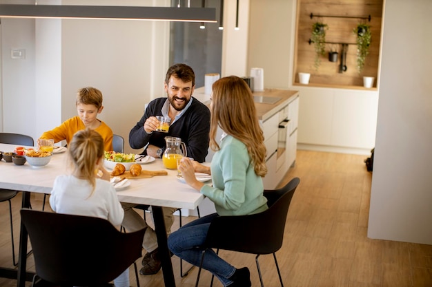 Foto família feliz conversando enquanto toma o café da manhã na mesa de jantar no apartamento