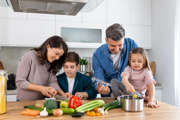 Família feliz cozinhando juntos na cozinha Mãe Filho e filha com o pai cozinhando Filho e mãe cortando legumes verdes Recreação em casa e preparação de comida no fim de semana