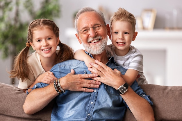 Família feliz crianças alegres abraçando o avô enquanto sentados juntos no sofá e olhando para a câmera no dia dos avós