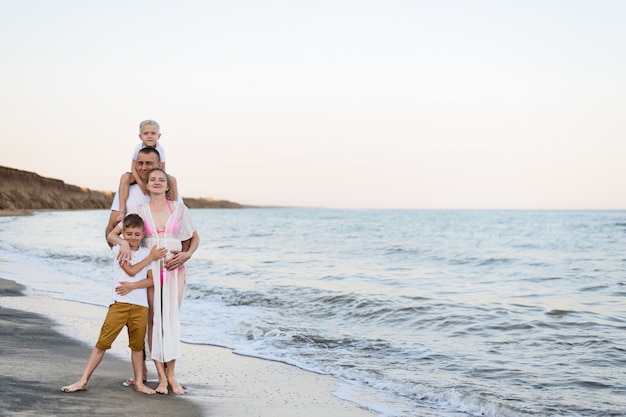 Familia feliz de cuatro abrazos en la costa del mar, padres, madre embarazada y dos hijos,