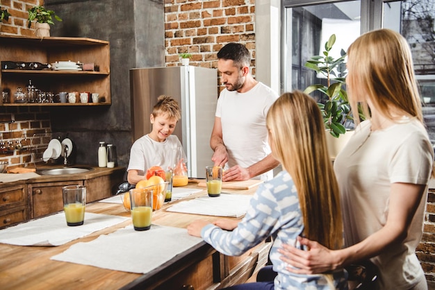 Familia feliz de cuatro hace jugo de naranja para el desayuno en la cocina