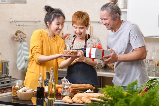 Família feliz da mãe pai e filha na cozinha comemorando a festa de aniversário com bolo e presente