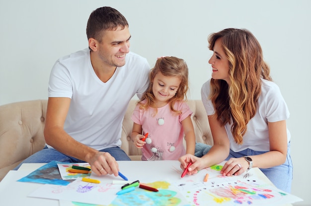 Família feliz de aparência Europeia. Sorrindo pais jogar e aprender a desenhar sua menina bonitinha.