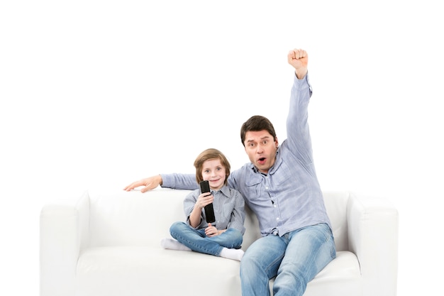 Família feliz de duas pessoas, fãs pai e filho no sofá com o controle remoto da TV
