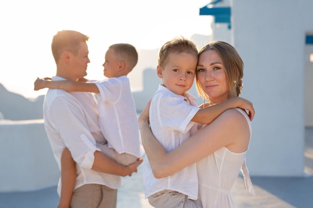 Família feliz de férias em Santorini Grécia Os pais seguram seus filhos nos braços