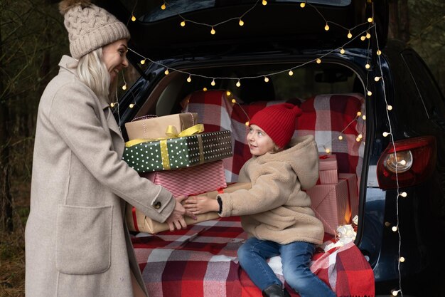 Família feliz de mãe e filha com caixas de presente de natal sentadas em carro decorado de natal