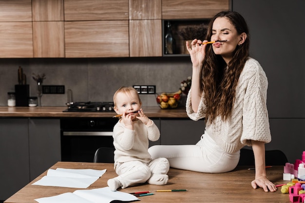 Família feliz de mãe e filha rindo e brincando com lápis de cor enquanto desenha Maternidade deixa Mãe e filha brincam e brincam juntas na cozinha em casa