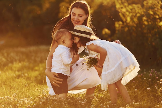 Família feliz de mãe filho e filha passando tempo livre no prado na hora do dia ensolarado de verão