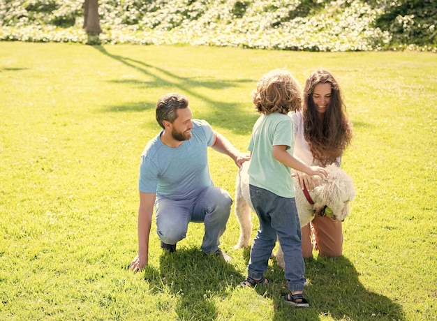 Família feliz de mãe pai e filho filho brincando com cachorro de estimação no parque de verão divertido grama verde