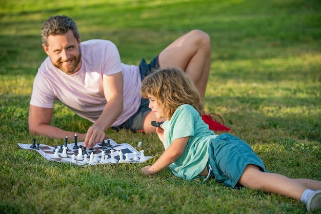 Família feliz de pai e filho filho jogando xadrez na grama verde no parque ao ar livre, xeque-mate.