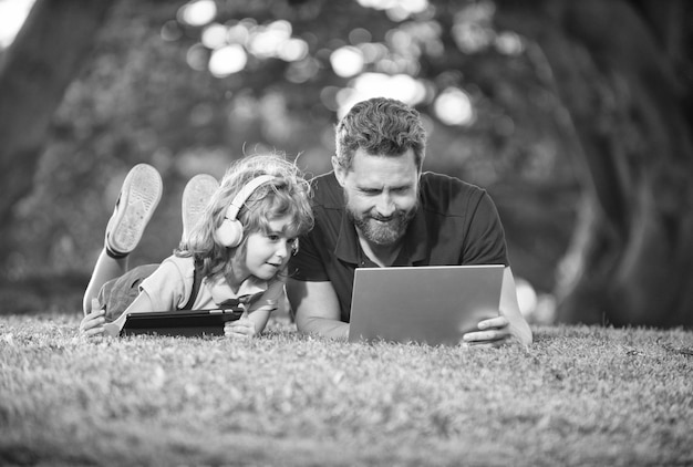 Família feliz de pai e filho usa laptop e fones de ouvido no fim de semana da família do parque