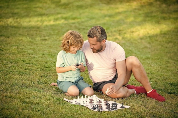 Família feliz de papai e filho jogando xadrez na grama verde no parque decisão ao ar livre