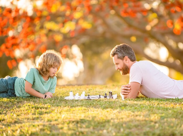 Família feliz de papai e filho jogando xadrez na grama verde no parque gênio ao ar livre