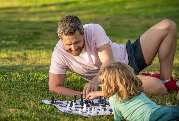 Família feliz de papai e filho jogando xadrez na grama verde no tabuleiro de xadrez ao ar livre do parque