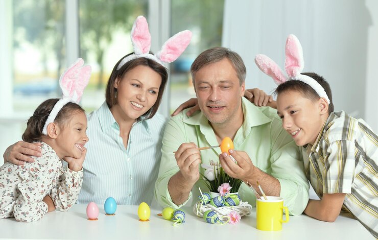 Foto família feliz de quatro usando orelhas de coelho e pintando ovos de páscoa em casa