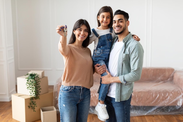 Família feliz de três pessoas mostrando as chaves de seu apartamento