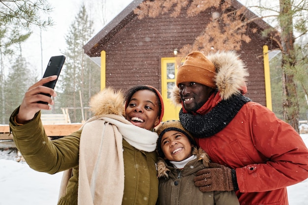 Família feliz de três posando para selfie no país em dia de inverno nevado