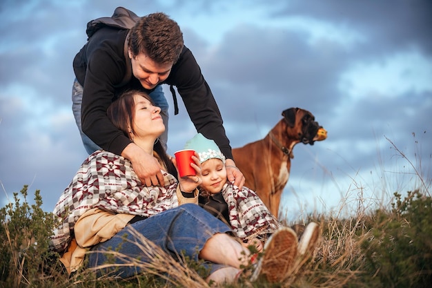 família feliz de viajantes, um homem cobre com um cobertor e abraça sua esposa e filha na natureza