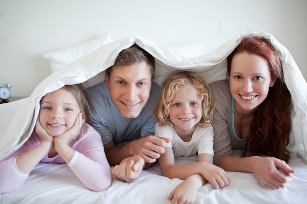 Familia feliz debajo de la cubierta de la cama