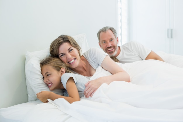 Família feliz deitada na cama no quarto de casa