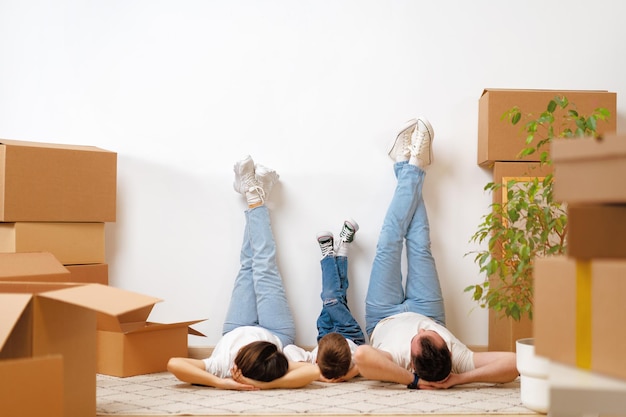 Família feliz deitada no chão em nova casa com caixas de cordas ao redor