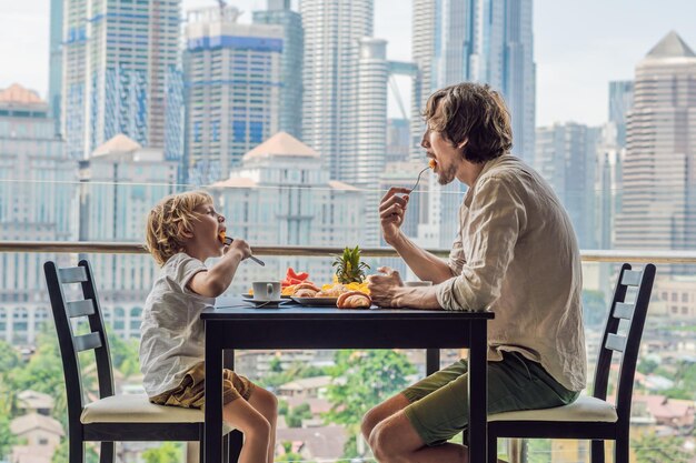 Familia feliz desayunando en el balcón mesa de desayuno con café, fruta y pan croisant en