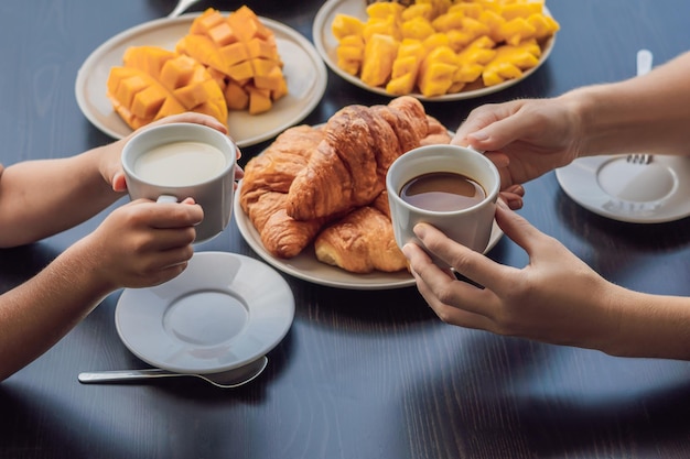 Familia feliz desayunando en el balcón. Mesa de desayuno con croisant de pan y fruta de café en un balcón con el telón de fondo de la gran ciudad