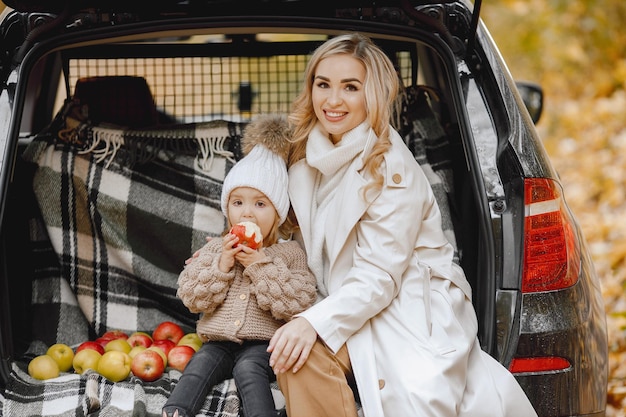 Família feliz descansando após o dia passar ao ar livre no parque outono. mãe e sua filha sentada dentro do porta-malas do carro, sorrindo. férias em família e conceito de viagem.