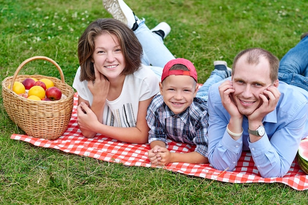 Família feliz descansando na natureza. Mãe, pai e filho, desfrutando e mentindo na manta quadriculada no Prado.