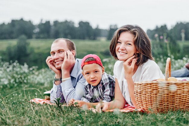 Família feliz descansando na natureza. Mãe, pai e filho, desfrutando e mentindo na manta quadriculada no Prado.