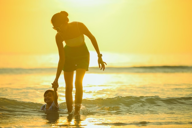 Família feliz descansando na praia no verão Pés de mãe e bebê na espuma do mar à luz do sol, a água está se movendo