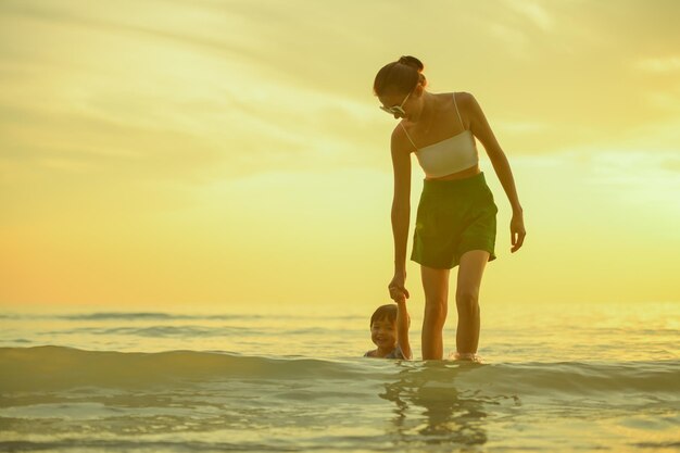 Foto família feliz descansando na praia no verão pés de mãe e bebê na espuma do mar à luz do sol, a água está se movendo