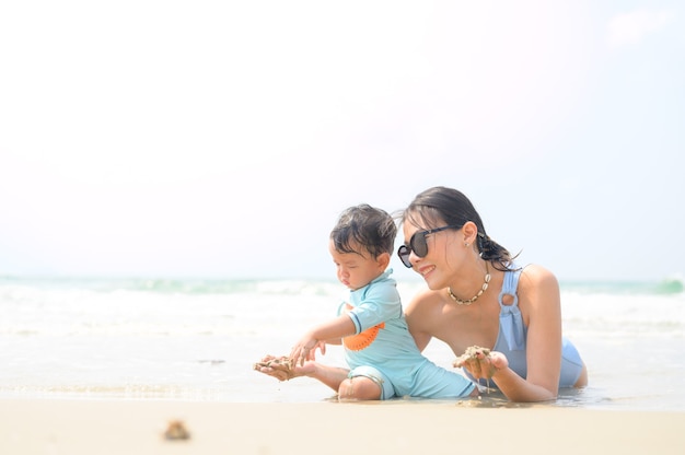 Foto familia feliz descansando en la playa en verano, los pies de la madre y el bebé en la espuma del mar en la luz del sol el agua se mueve