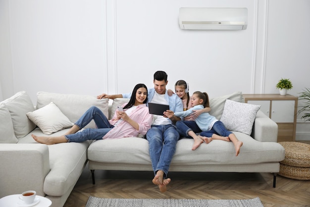 Família feliz descansando sob ar condicionado na parede branca em casa