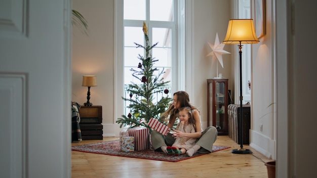 Familia feliz desempacando regalos en casa acogedora Mamá hija pasando Navidad