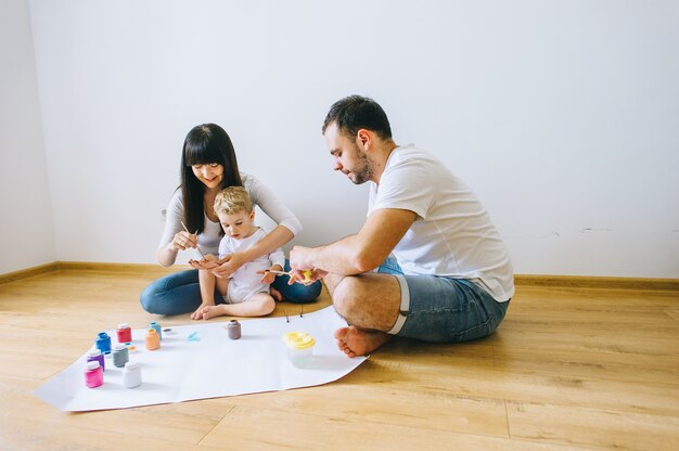 Familia feliz dibujando sobre papel en el piso de parquet con un gato