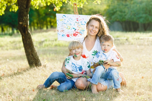 Familia feliz dibujo al aire libre. Joven madre divirtiéndose con sus hijos pequeños
