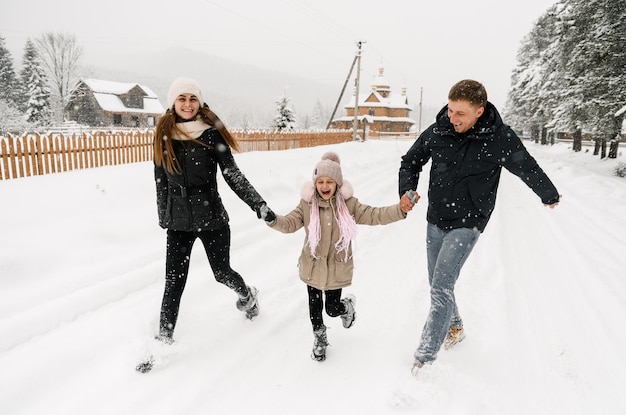 Familia feliz divertirse en el bosque de invierno. Madre, padre e hija jugando con la nieve. Disfrutando de pasar tiempo juntos. Concepto de familia