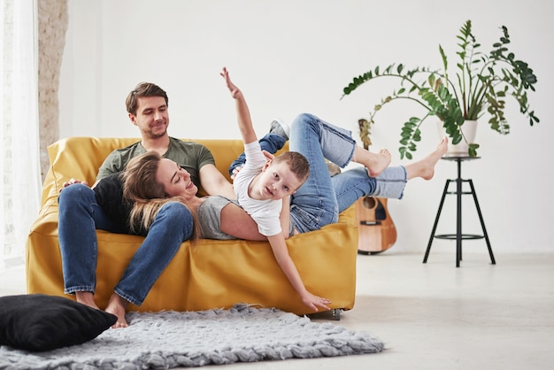 La familia feliz se divierte en el sofá amarillo del salón de su nueva casa.