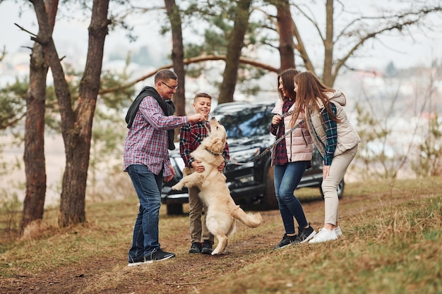 La familia feliz se divierte con su perro activo cerca de un camión moderno al aire libre en el bosque