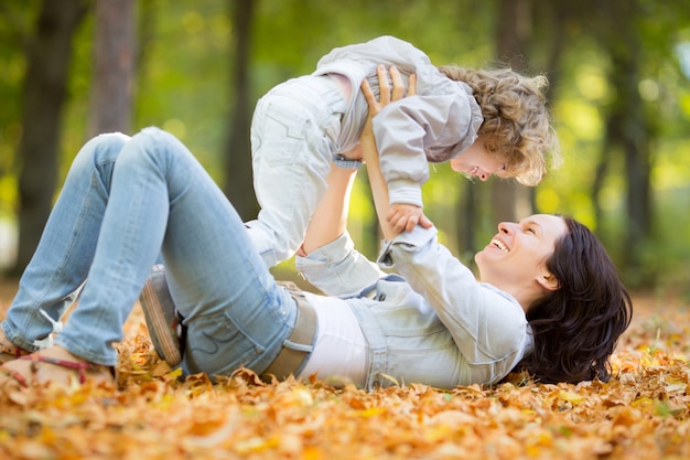 Familia feliz divirtiéndose al aire libre en el parque de otoño contra el fondo de hojas borrosas