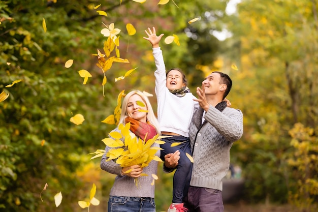 Familia feliz divirtiéndose al aire libre en el parque de otoño contra el fondo de hojas borrosas