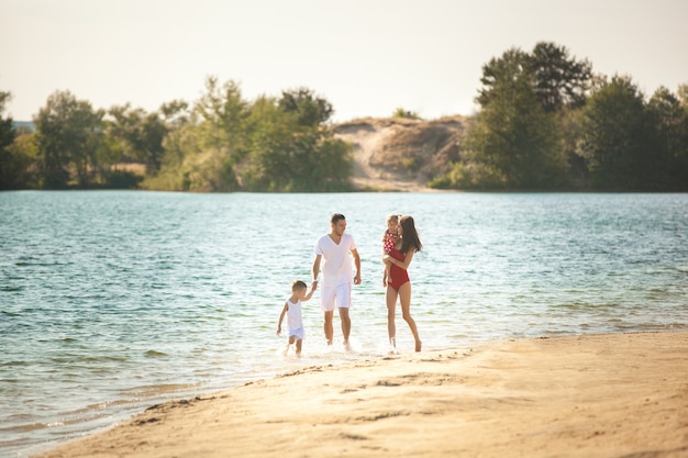 Familia feliz divirtiéndose en la playa. Mamá, papá, hijo e hija pequeña en la orilla del mar. Familia alegre