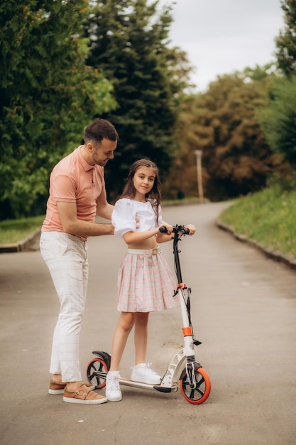 Família feliz e amigável de pai e menina pré-adolescente andando de scooter ao ar livre na floresta Foto de alta qualidade