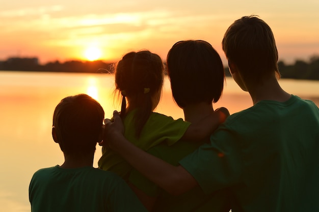 Família feliz e amigável perto do rio contra o pôr do sol