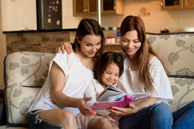 Família feliz e amorosa. Muito jovem mãe e sua irmã lendo um livro para a filha.