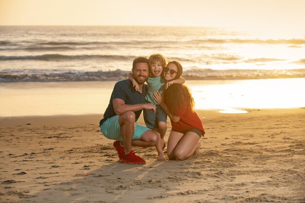 Família feliz e criança curtindo o pôr do sol na praia, lazer de verão