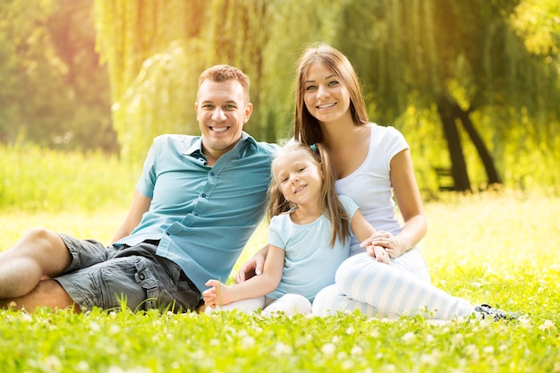 Família feliz e sorridente, sentado na grama do parque e olhando para a câmera.