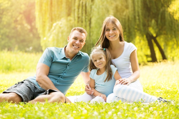 Família feliz e sorridente, sentado na grama do parque e olhando para a câmera.