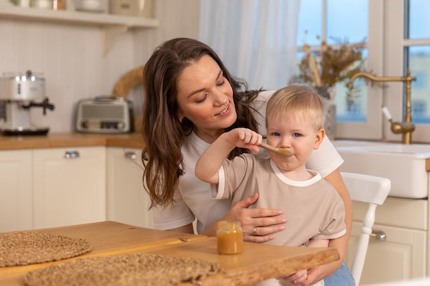 Família feliz em casa mãe alimentando bebê na cozinha garotinho com cara engraçada bagunçada come fo